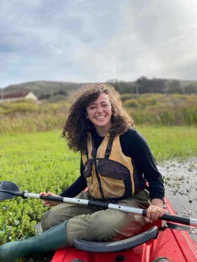 a woman holds a paddle sitting on a kayak