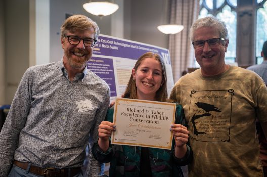 woman holds award with two men