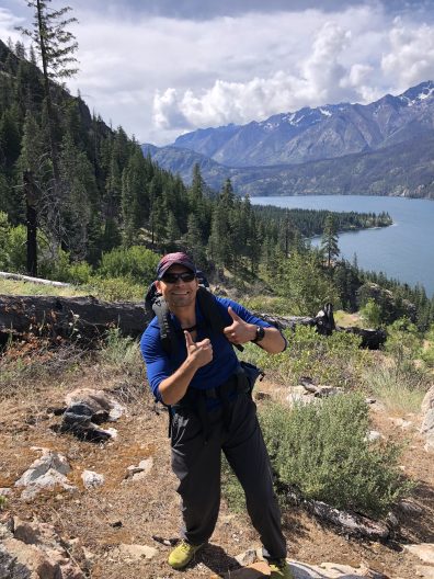 man stands near forested mountains and a lake