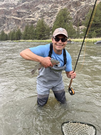 man wearing waders holds fish and pole