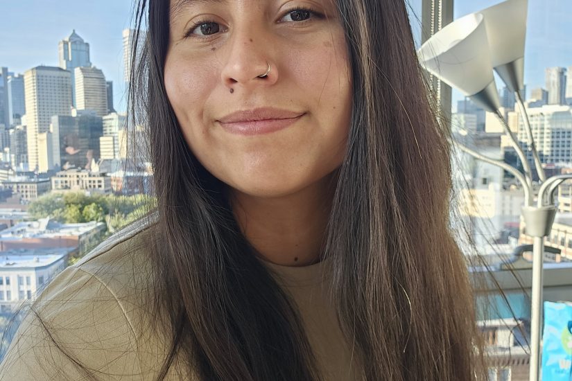 A woman in a tan shirt with a cityscape in the background.