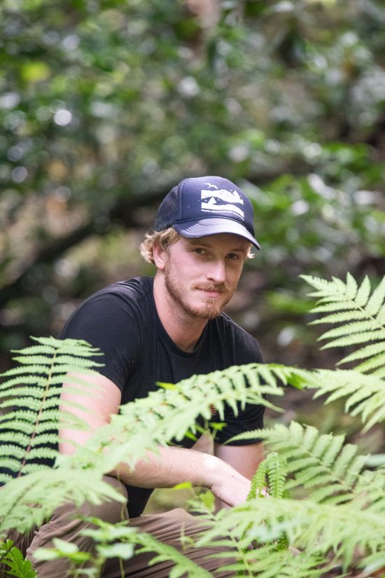 Man in hat stands behind ferns