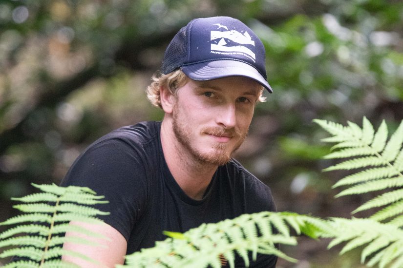 Man in hat stands behind ferns