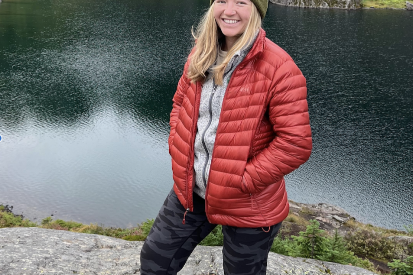 Woman in red puffer jacket stands in front of lake.