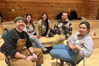Students sit in a circle at a holiday party with a wood paneled background.
