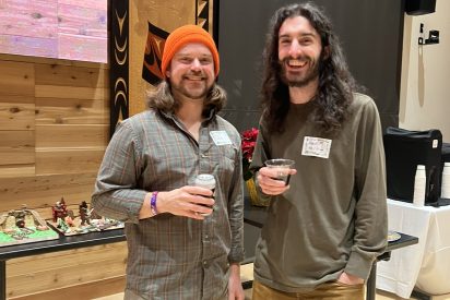 Two students smile for the camera at a holiday party with a wood paneled background.