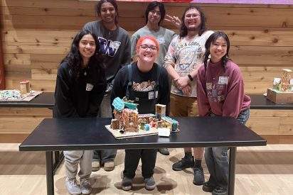Students pose in front of a gingerbread house.