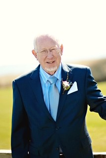 A man in a blue suit smiles for the camera with green grass in the background.