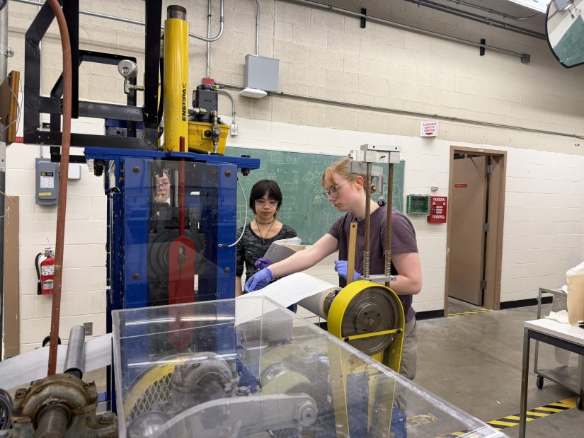 Kira Stewart (right) and Alaina Duque assist one another in operating the Wollenberg Lab's paper machine in Bloedel Hall. 